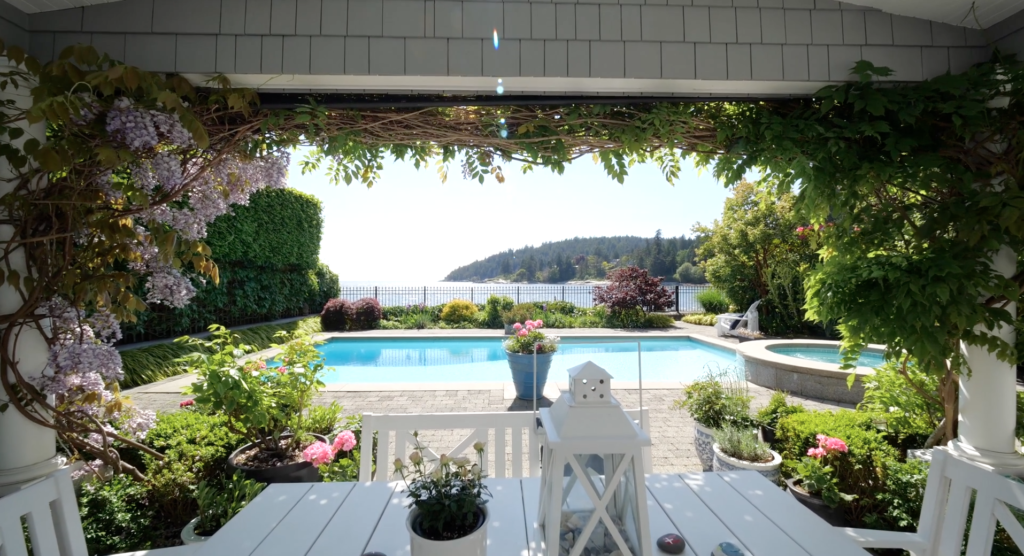 a pool with a deck and a table with plants and a fence